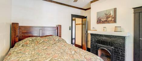 A bedroom with a wooden headboard, a large floral bedspread, a fireplace, and a ceiling fan.