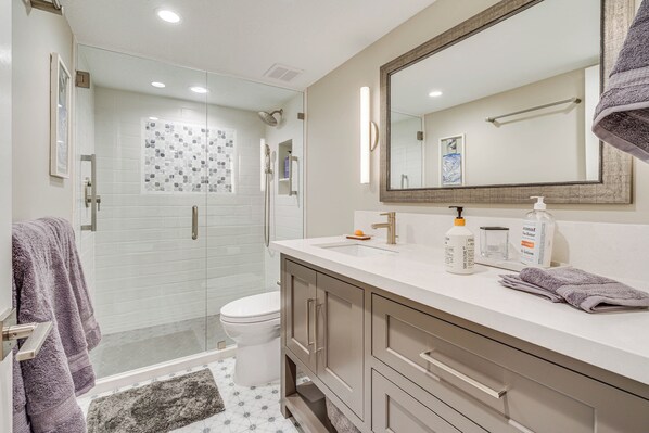 Un baño moderno con cabina de ducha de vidrio, inodoro blanco y tocador con espejo.
