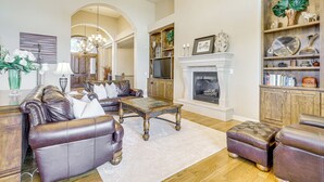 A spacious living room with leather sofas, a fireplace, wooden shelves, and a chandelier. - Game Room & Deck: Group Getaway in New Mexico! (Tucumcari)