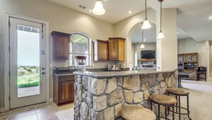 A spacious kitchen with a stone island, wooden cabinets, and bar stools. - Game Room & Deck: Group Getaway in New Mexico! (Tucumcari)