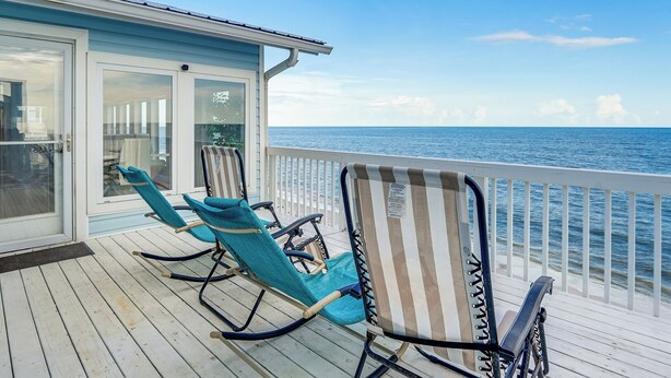 Une terrasse avec deux fauteuils à bascule et une chaise à rayures, donnant sur l’océan.