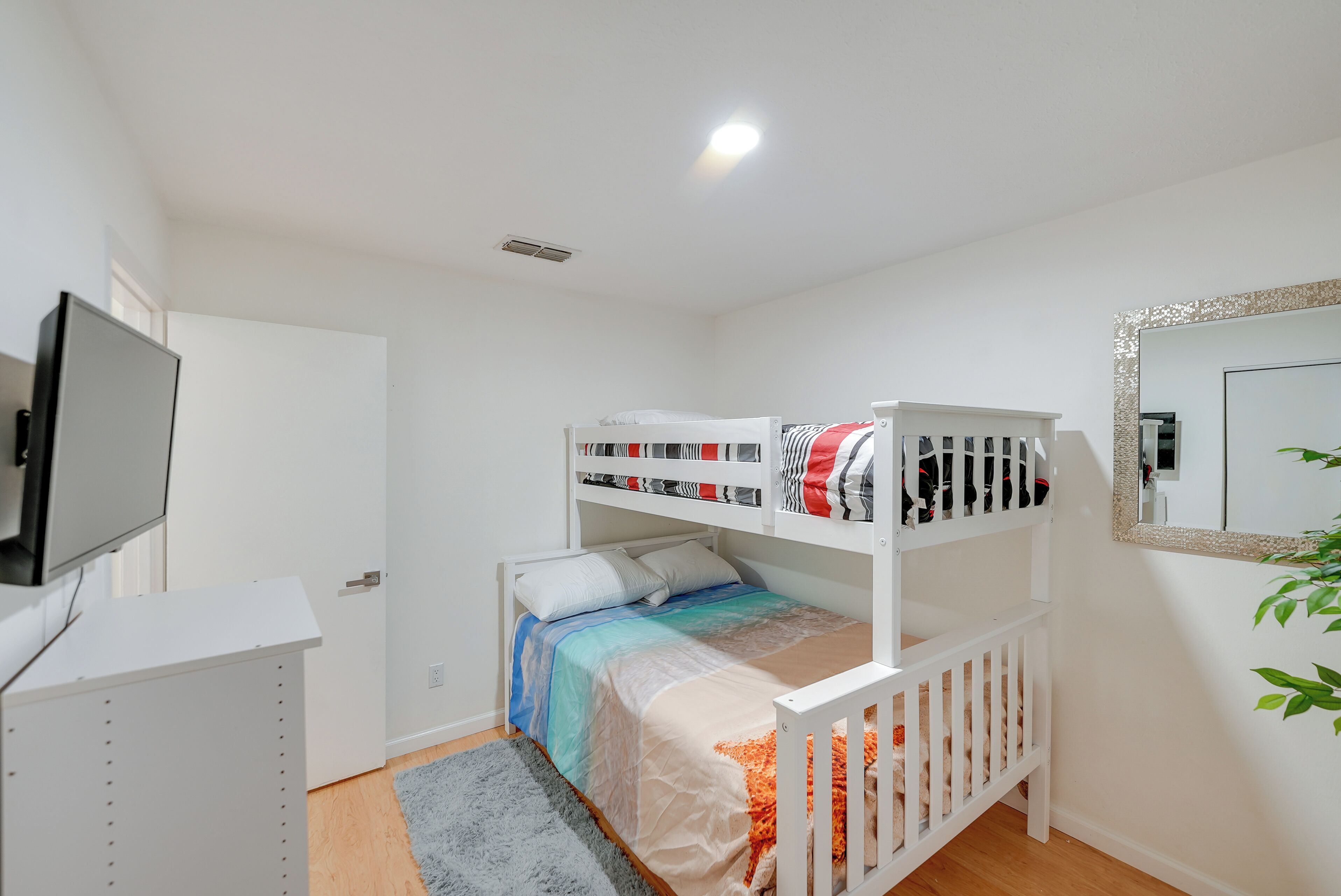 A bunk bed with a TV on a stand, a desk, and a mirror on the wall.
