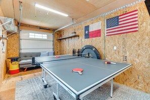 A ping pong table in a room with wooden walls, two American flags, and a gray couch. - Sunset Cove Lakefront Rental w/ Private Dock! (Onalaska)