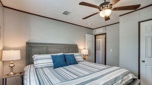 A neatly made bed with striped bedding and two pillows, a ceiling fan, and bedside lamps. - Sunset Cove Lakefront Rental w/ Private Dock! (Onalaska)
