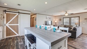 A kitchen with a wooden barn-style door, a central island with chairs, a dining table, and a ceiling fan. - Sunset Cove Lakefront Rental w/ Private Dock! (Onalaska)