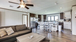 A modern kitchen with white cabinets, a stainless steel refrigerator, and a dining area with white chairs. - Sunset Cove Lakefront Rental w/ Private Dock! (Onalaska)