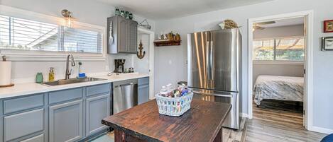 A kitchen with grey cabinets, a stainless steel refrigerator, and a wooden table with a basket of items.