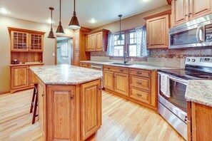 A spacious kitchen with wooden cabinets, a granite countertop, stainless steel appliances, and a large island. - Charming Tonica Farmhouse w/ Private Yard! (Tonica)