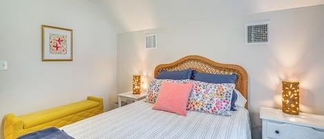 Un dormitorio con cama, mesitas de noche, un banco, un ventilador de techo, una lámpara de pared y una ventana.