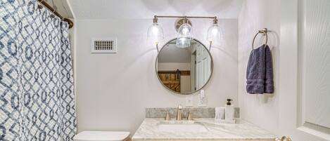 A bathroom with a toilet, sink, vanity, and a mirror with lights.