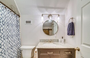 Un baño con inodoro, lavamanos, tocador y espejo con luces.