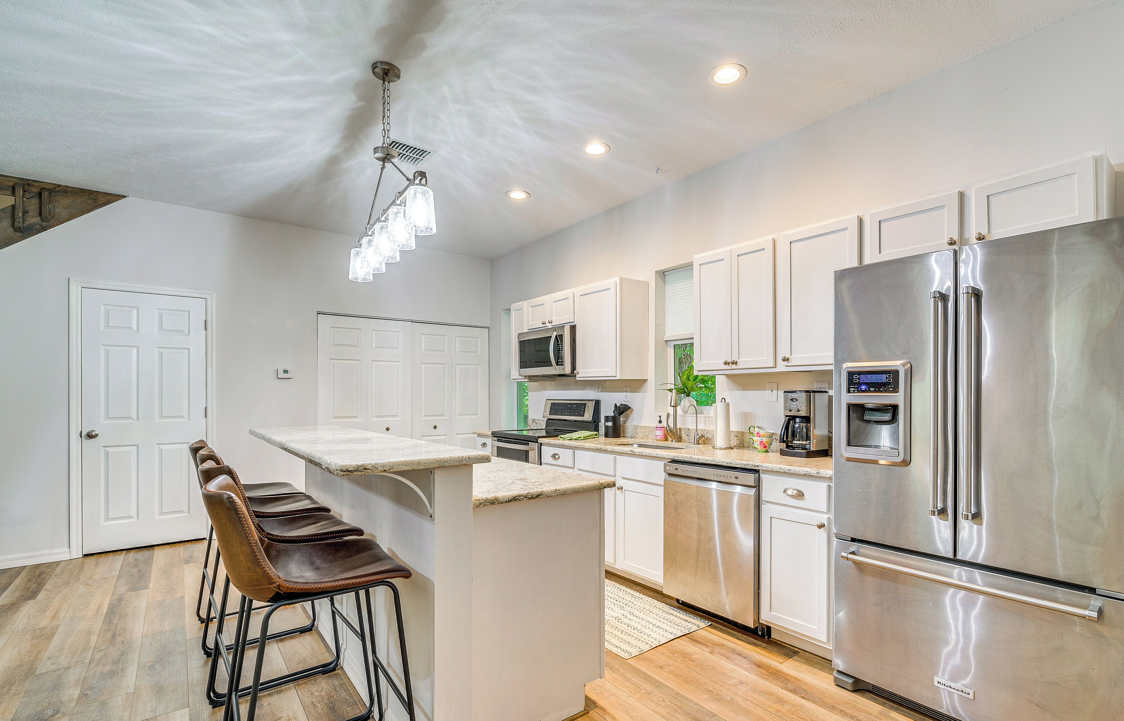 A modern kitchen with white cabinets, stainless steel appliances, and a bar area with stools.