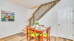 A dining area with a wooden table set for four, surrounded by chairs with green cushions, a white door, and a staircase with wooden railings. - 3 Mi to Silver Springs State Park: Cozy Getaway! (Silver Springs)