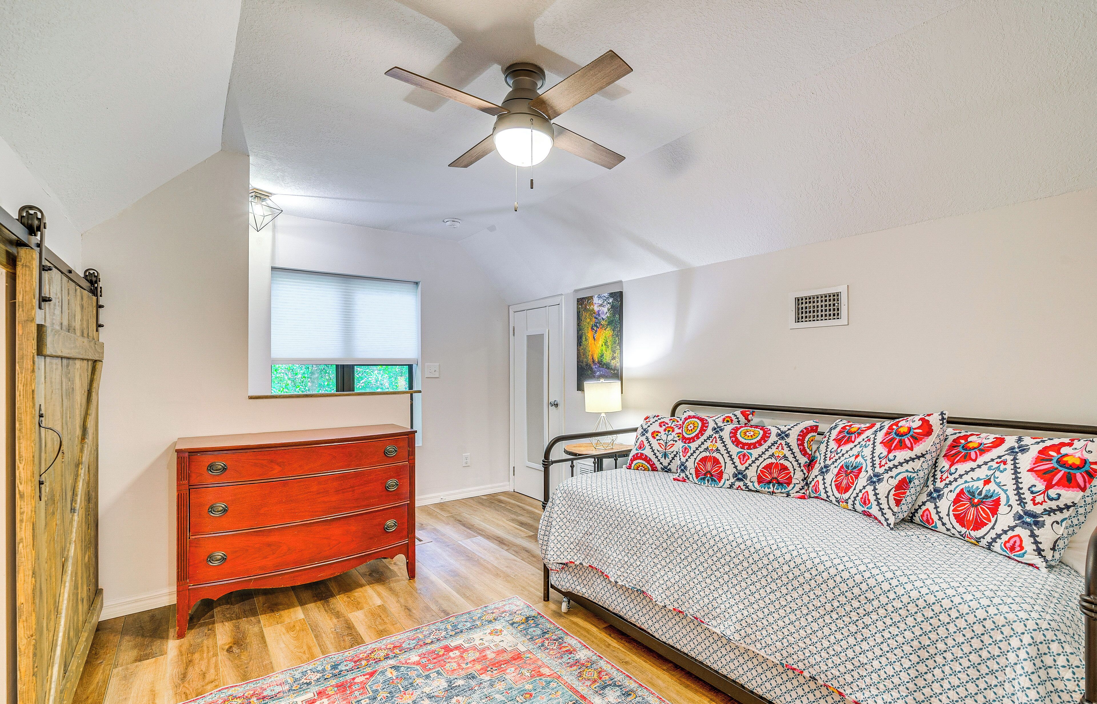 Une chambre à coucher comprenant un lit, une commode, un ventilateur de plafond, une fenêtre et une porte.