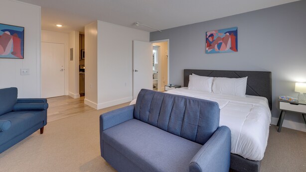 A modern hotel room with a large bed, a blue sofa, and artwork on the walls. - Studio in Gadsden ~ 10 Mi to the Coosa River! (Gadsden)