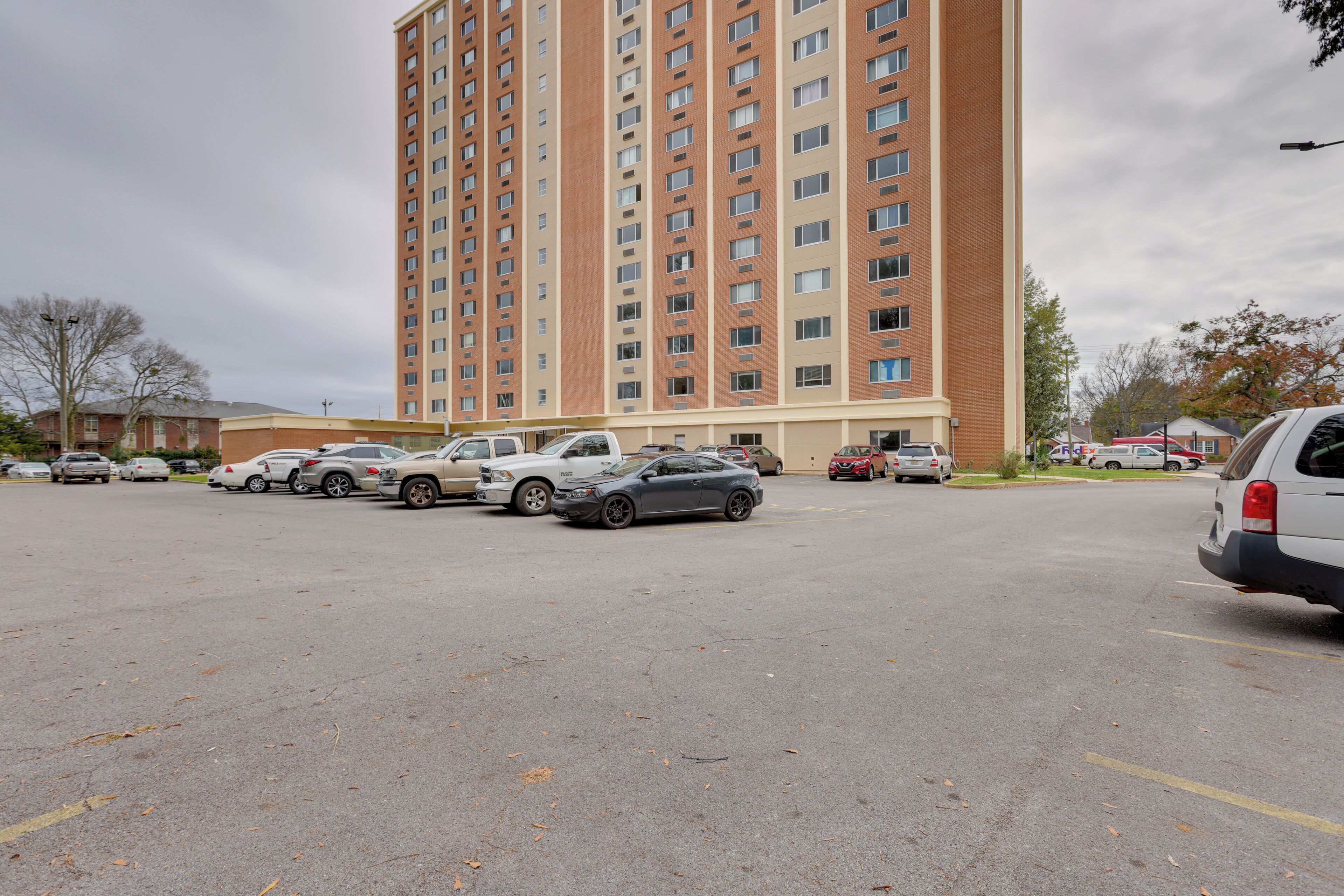 A parking lot with several cars and a tall residential building in the background.