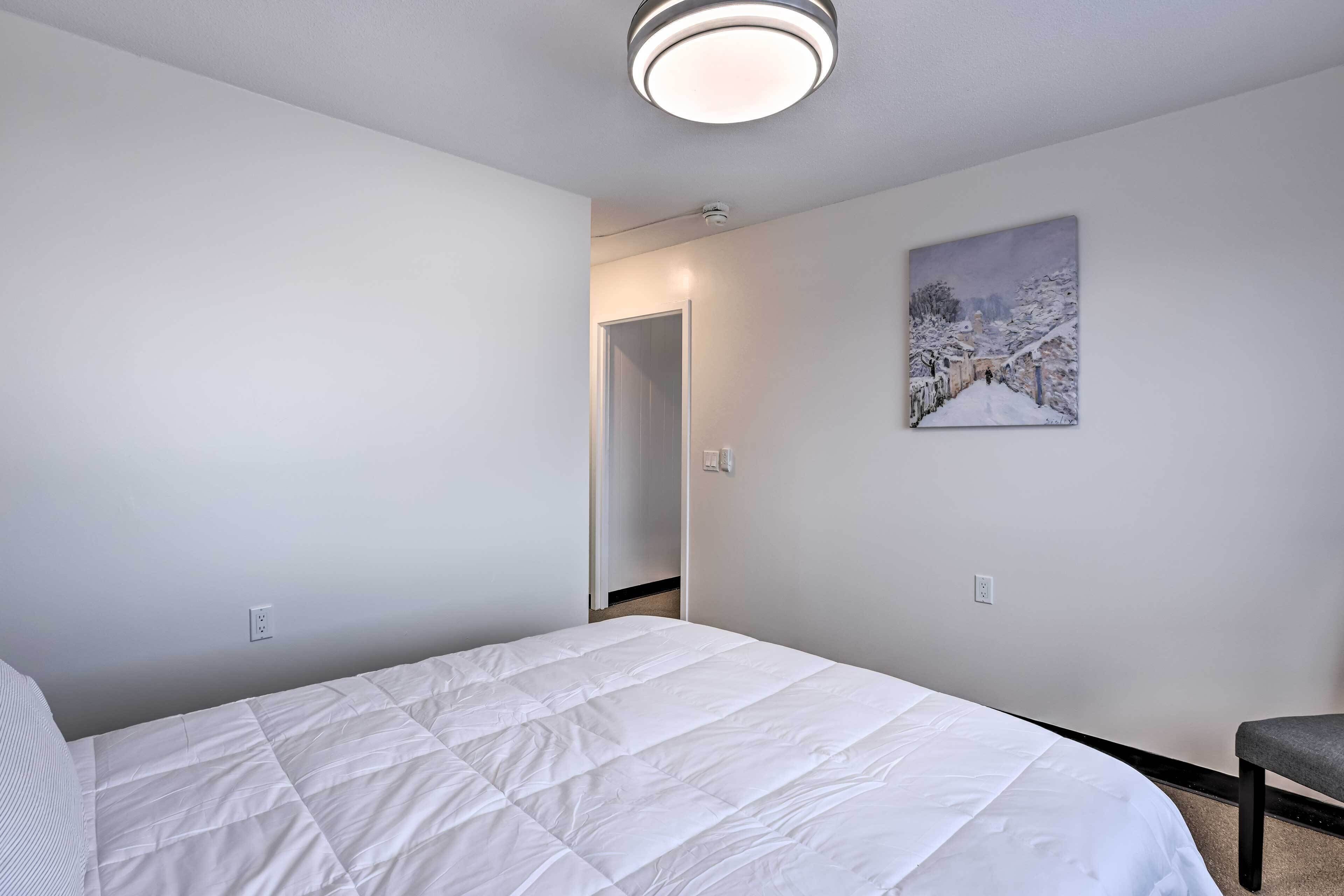 Une chambre avec un lit blanc, un tableau représentant un paysage enneigé et une chaise.