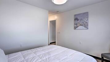 Une chambre avec un lit blanc, un tableau représentant un paysage enneigé et une chaise.