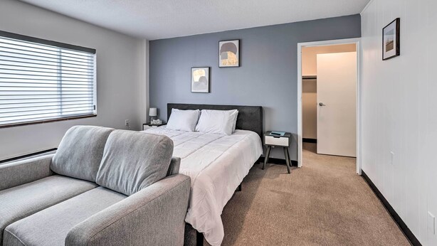 A bedroom with a bed, a nightstand, a chair, and a door leading to another room. - Airy Apt Situated in the Coosa River Area! (Gadsden)