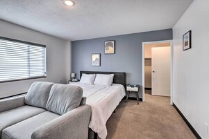A bedroom with a bed, a nightstand, a chair, and a door leading to another room.