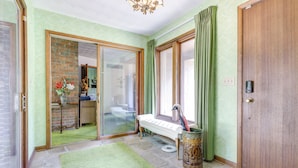 Una habitación con alfombra verde, un banco, una urna decorativa y una puerta de madera.