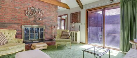A living room with a brick fireplace, a sofa, a chair, and a glass coffee table.