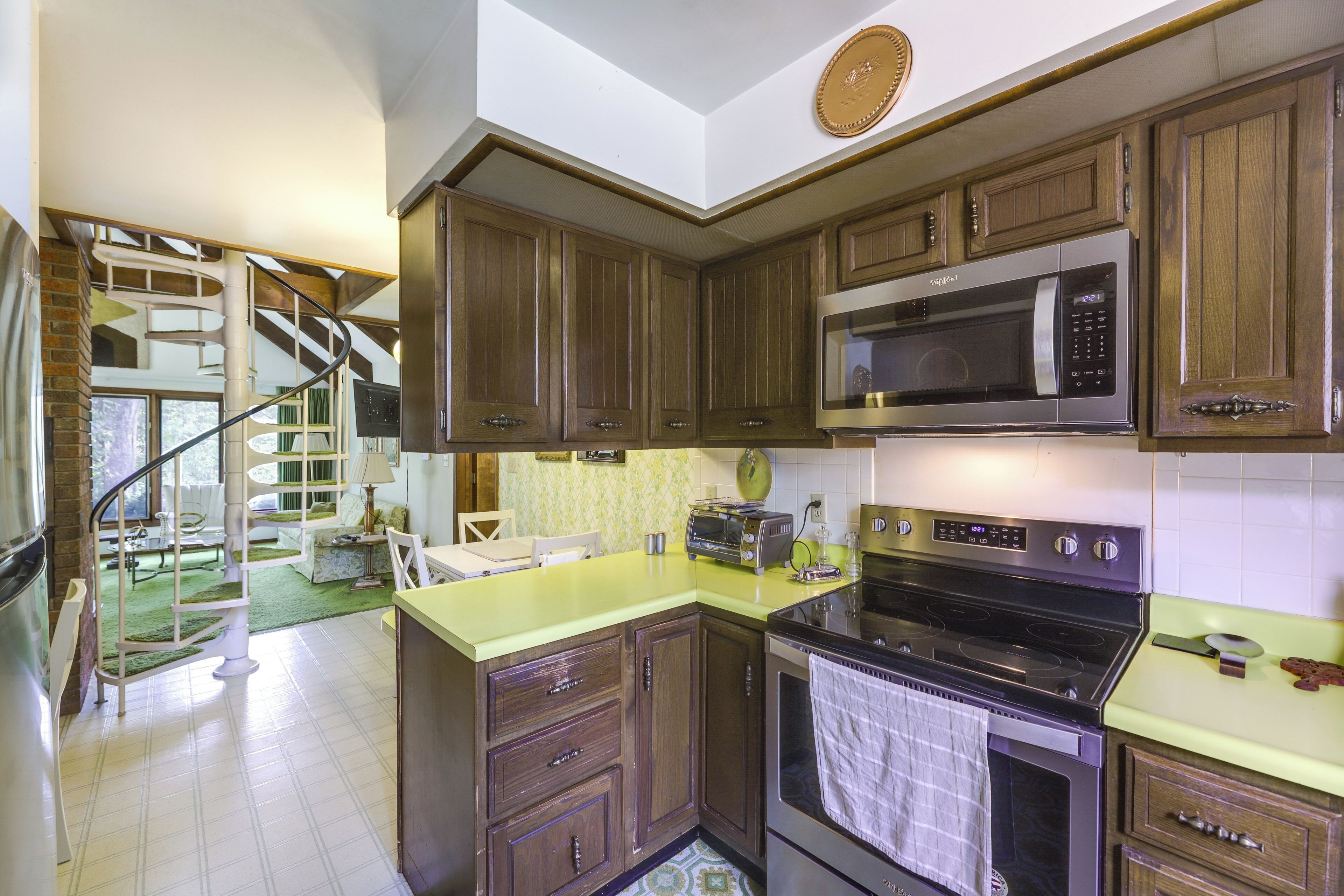 A kitchen with wooden cabinets, a microwave, a stove, and a spiral staircase leading to a dining area.