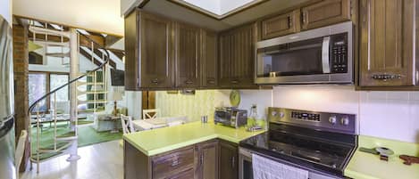 A kitchen with wooden cabinets, a microwave, a stove, and a spiral staircase leading to a dining area.