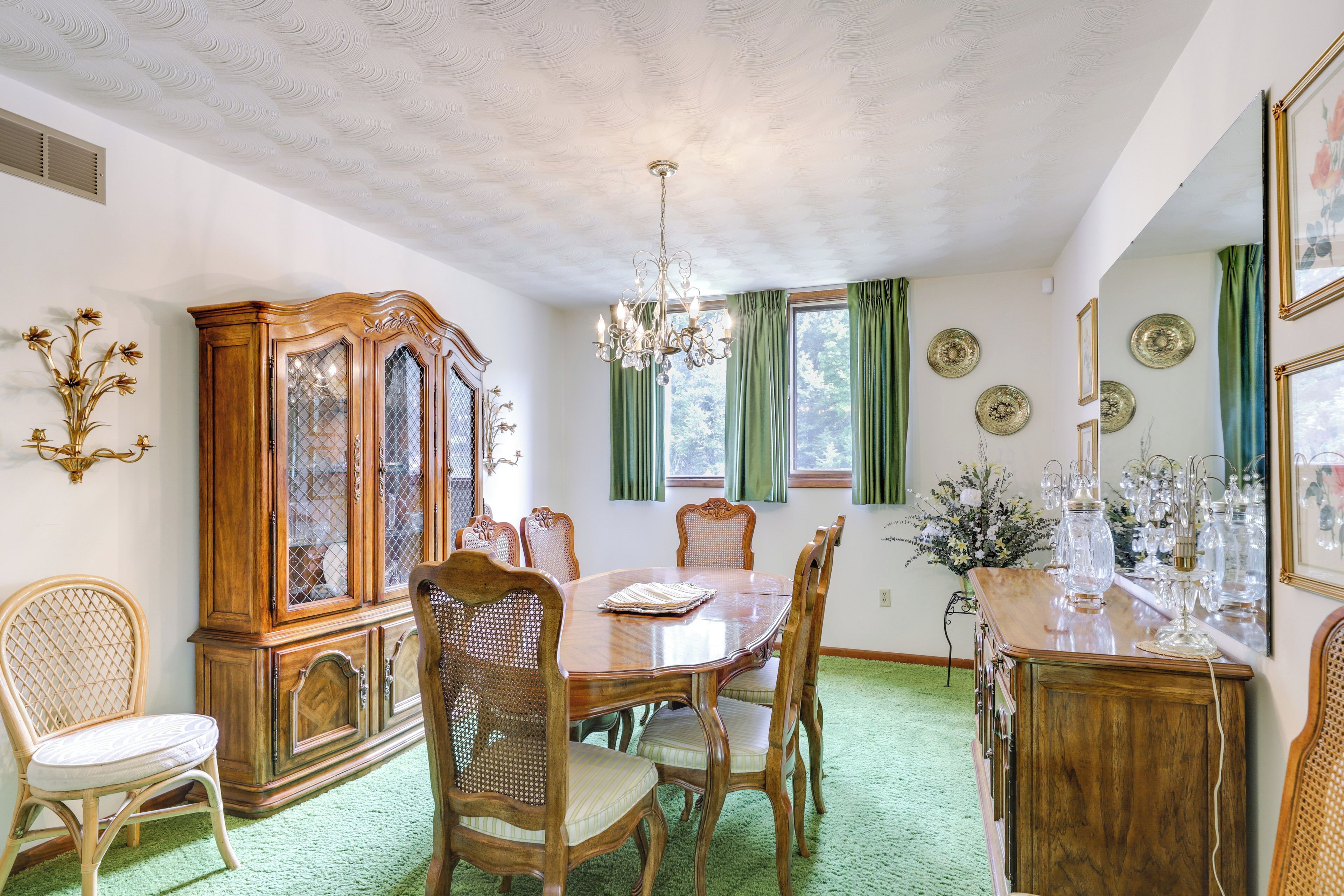 A dining room with a wooden table, chairs, a large cabinet, and a chandelier.
