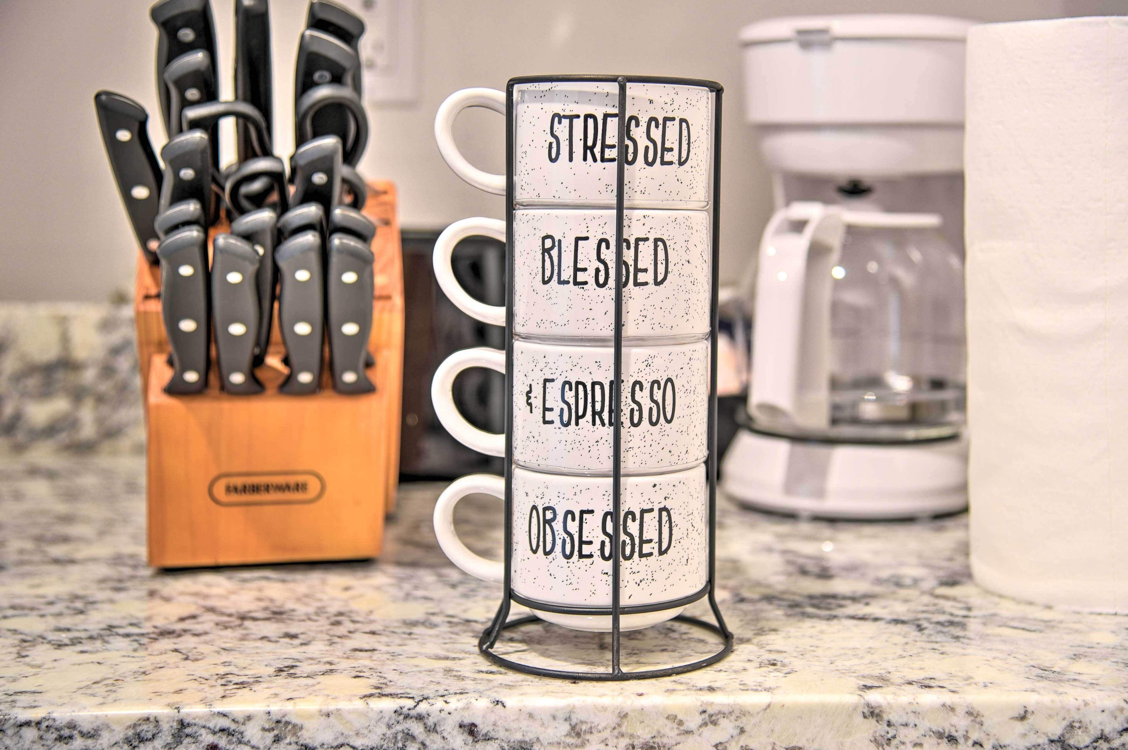Una encimera de cocina con un bloque de cuchillos, una cafetera y un escurreplatos con palabras como 'STRESSED', 'BLESSED', 'ESPRESSO' y 'OBSESSED'.