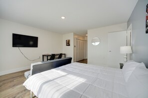 A hotel room with a large bed, a desk, a chair, a TV mounted on the wall, and a round mirror. - Bright Gadsden Apartment ~ 10 Mi to Dive Land Park (Gadsden)