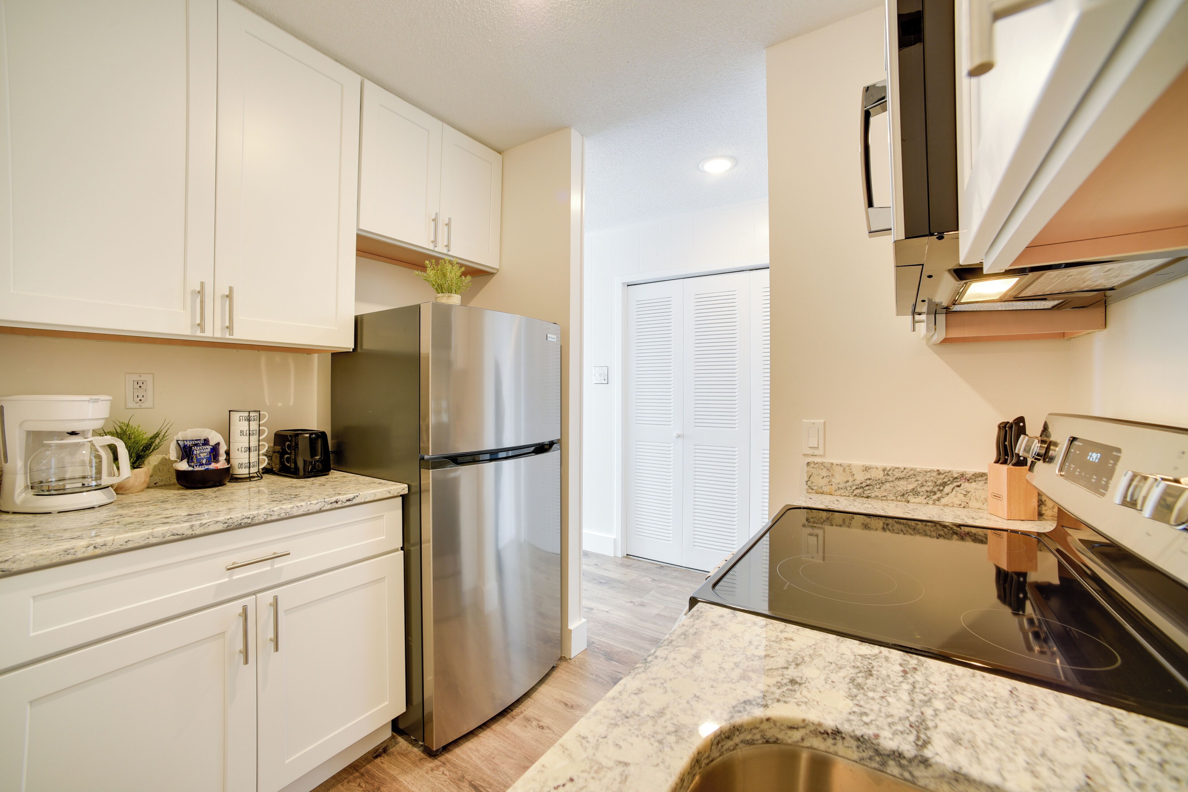 A modern kitchen with white cabinets, a stainless steel refrigerator, a built-in oven, and a granite countertop.