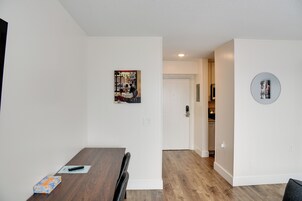 Un comedor moderno con una mesa y sillas de madera, un pequeño cuadro en la pared y una cocina visible al fondo.