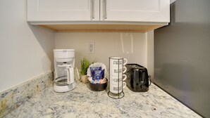 Cozinha com armários brancos, cafeteira, torradeira e suporte para canecas.