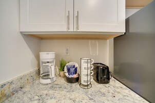 Una cocina con armarios blancos, una cafetera, un tostador y un escurreplatos para tazas.