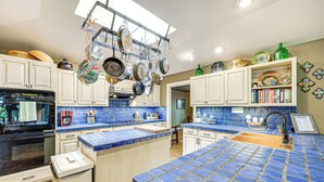 Een keuken met blauwe betegelde aanrechtbladen, hangende pannen en diverse keukengerei.
