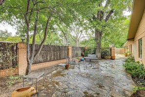 A stone patio with a table and chairs, surrounded by trees and a brick wall.