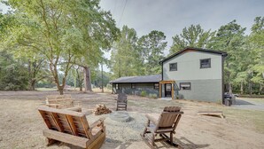 Un chalet rustique doté d’un porche couvert, entouré d’arbres et comprenant un espace avec foyer et des meubles en bois.