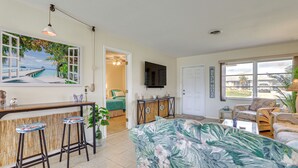 A living room with a bar area, a large window, and a tropical-themed painting. - Venice Home w/ Fenced Yard: 4 Mi to Beach! (Venice)