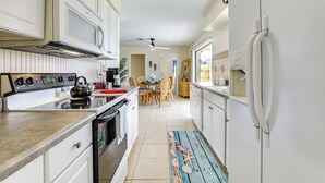 A kitchen with white cabinets, a stove, microwave, and refrigerator. There is a dining area with chairs and a table. - Venice Home w/ Fenced Yard: 4 Mi to Beach! (Venice)