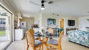 A spacious living area with a dining table surrounded by wicker chairs, a sofa with a tropical print, a ceiling fan, and a kitchen in the background. - Venice Home w/ Fenced Yard: 4 Mi to Beach! (Venice)