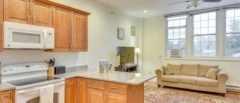 A kitchen with wooden cabinets, a microwave, stove, and a ceiling fan.