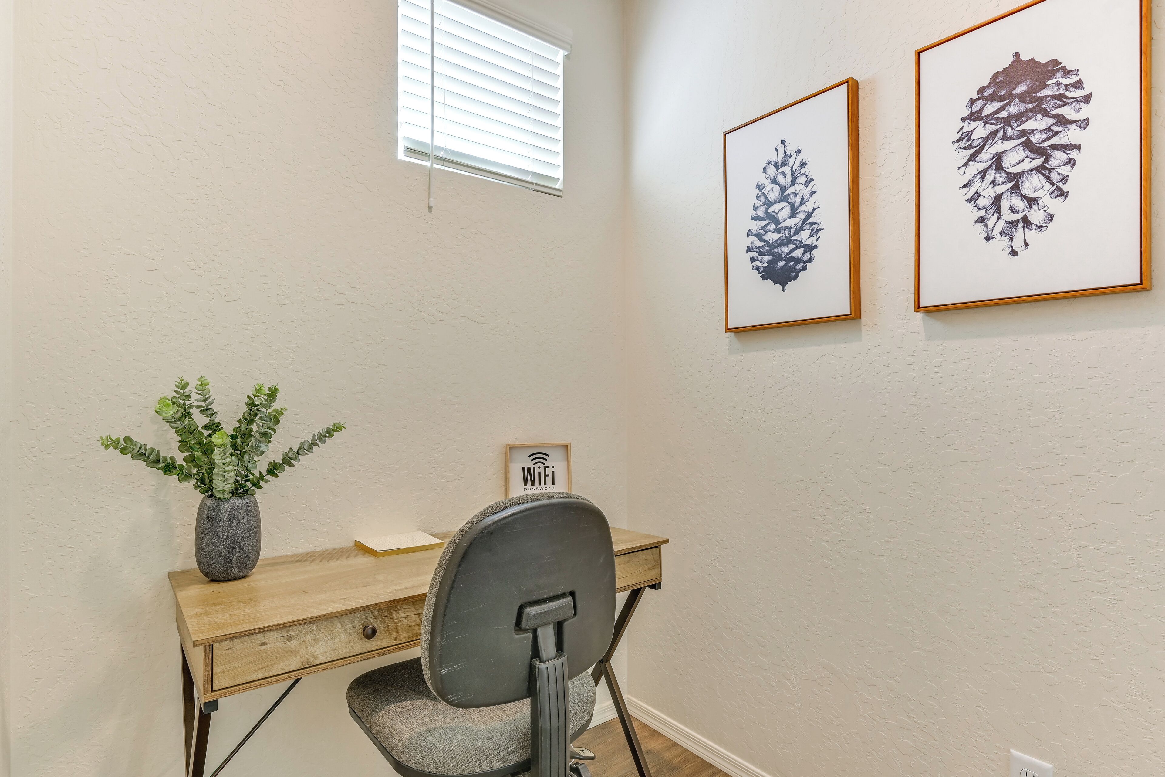 A home office with a desk, chair, framed artwork, and a potted plant.