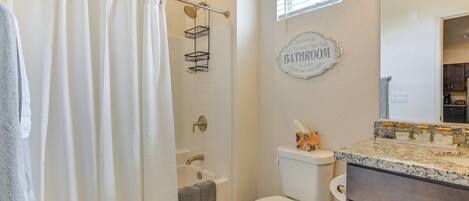 A bathroom with a shower curtain, a bathtub, a toilet, and a vanity with a mirror.
