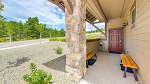 A covered porch with a stone pillar, a wooden bench, and a red door.