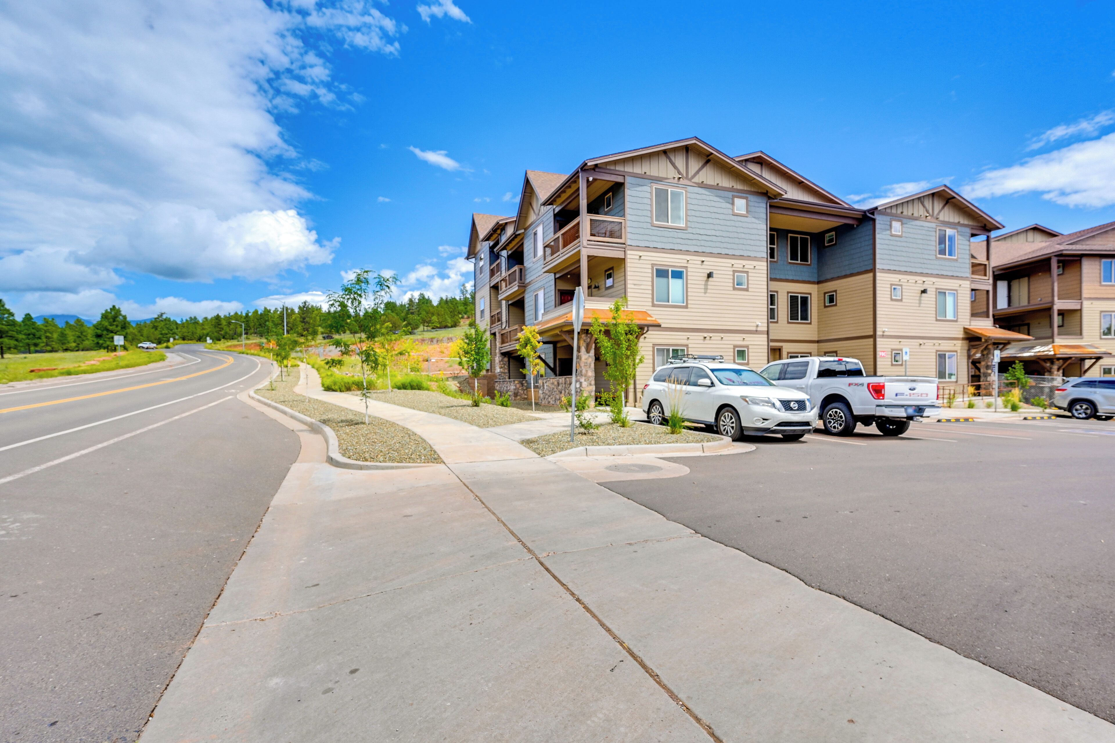 A multi-story residential building with balconies, a parking area, and a curved road.