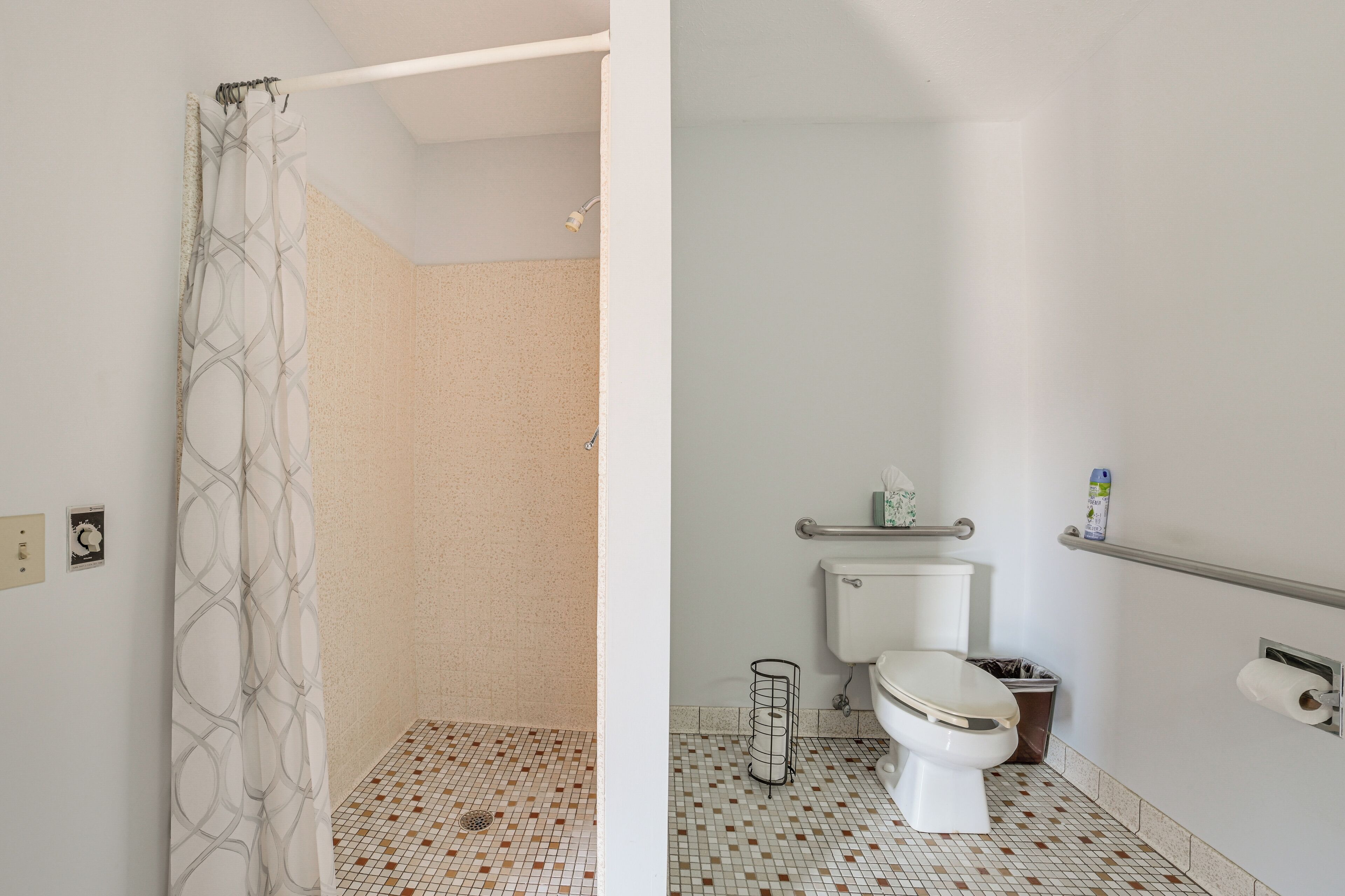 Une salle de bain équipée de toilettes, d’un rideau de douche, d’une barre d’appui et d’un sol carrelé.