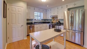 A kitchen with white cabinets, a stainless steel refrigerator, a wooden table, and a window with natural light. - Lakefront Lineville Retreat w/ Private Dock! (Lineville)