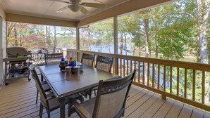 A covered outdoor deck with a table and chairs, a grill, and a view of a lake surrounded by trees. - Lakefront Lineville Retreat w/ Private Dock! (Lineville)