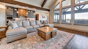A spacious living room with a sectional sofa, a wooden coffee table, and a large window providing a view. - Elegant 'sunset Meadow Ranch' in Texas w/ Hot Tub (Ponder)
